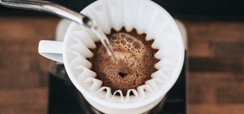 Top down view of hot water being poured into a corrugated cup-top filter paper full of dark brown coffee grounds